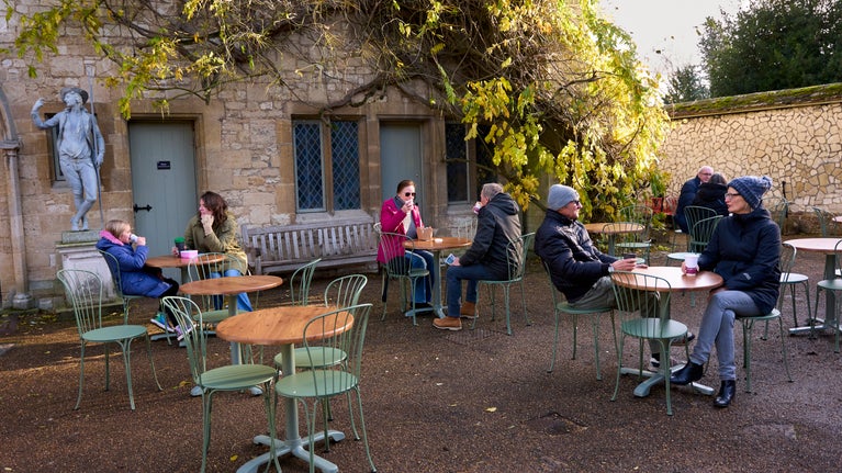 Groups of people sitting on tables in the courtyard outside the house. Wisteria lines the house wall.